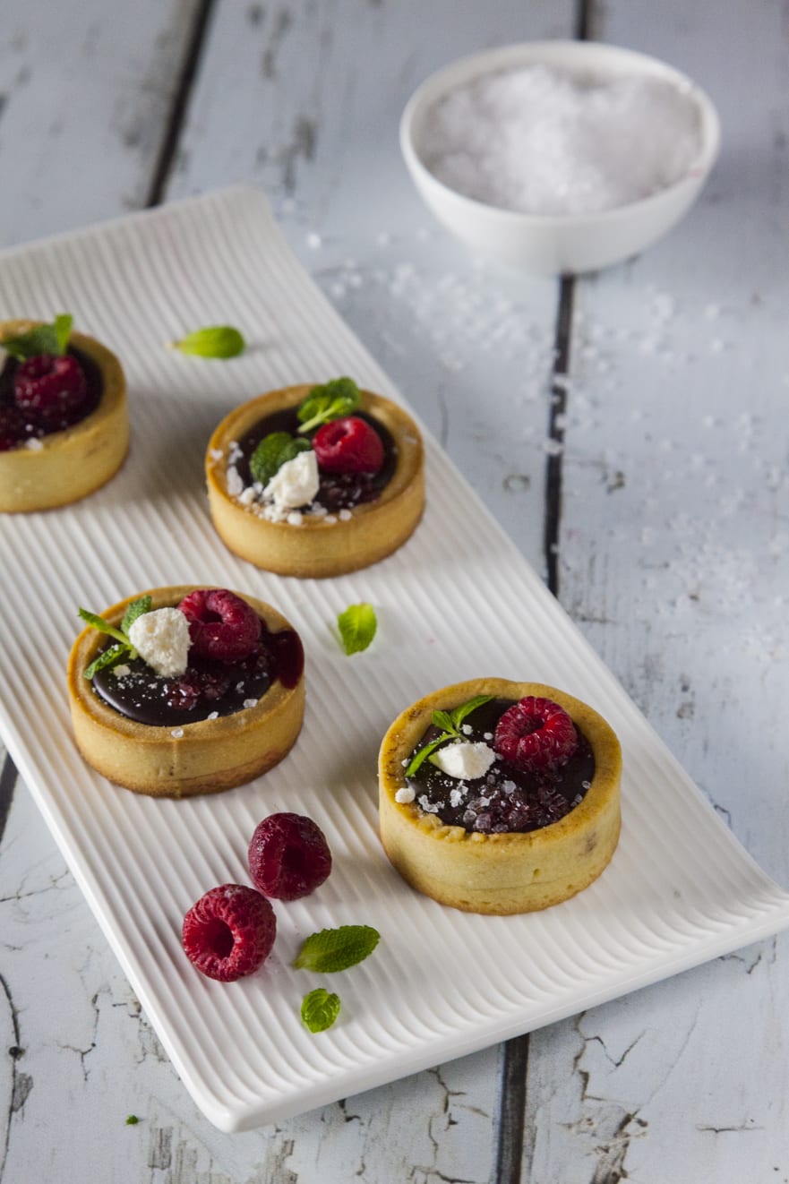 Tartellette con ganache al cioccolato e sale fino, cioccolata fondente e decorazioni con menta e lamponi