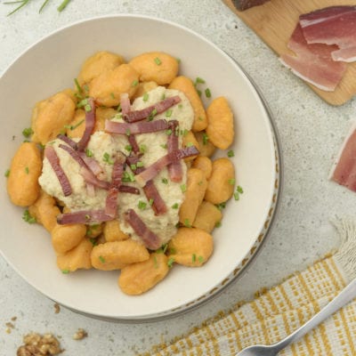 gnocchi di patate dolci serviti su piatto con speck e salsa di noci