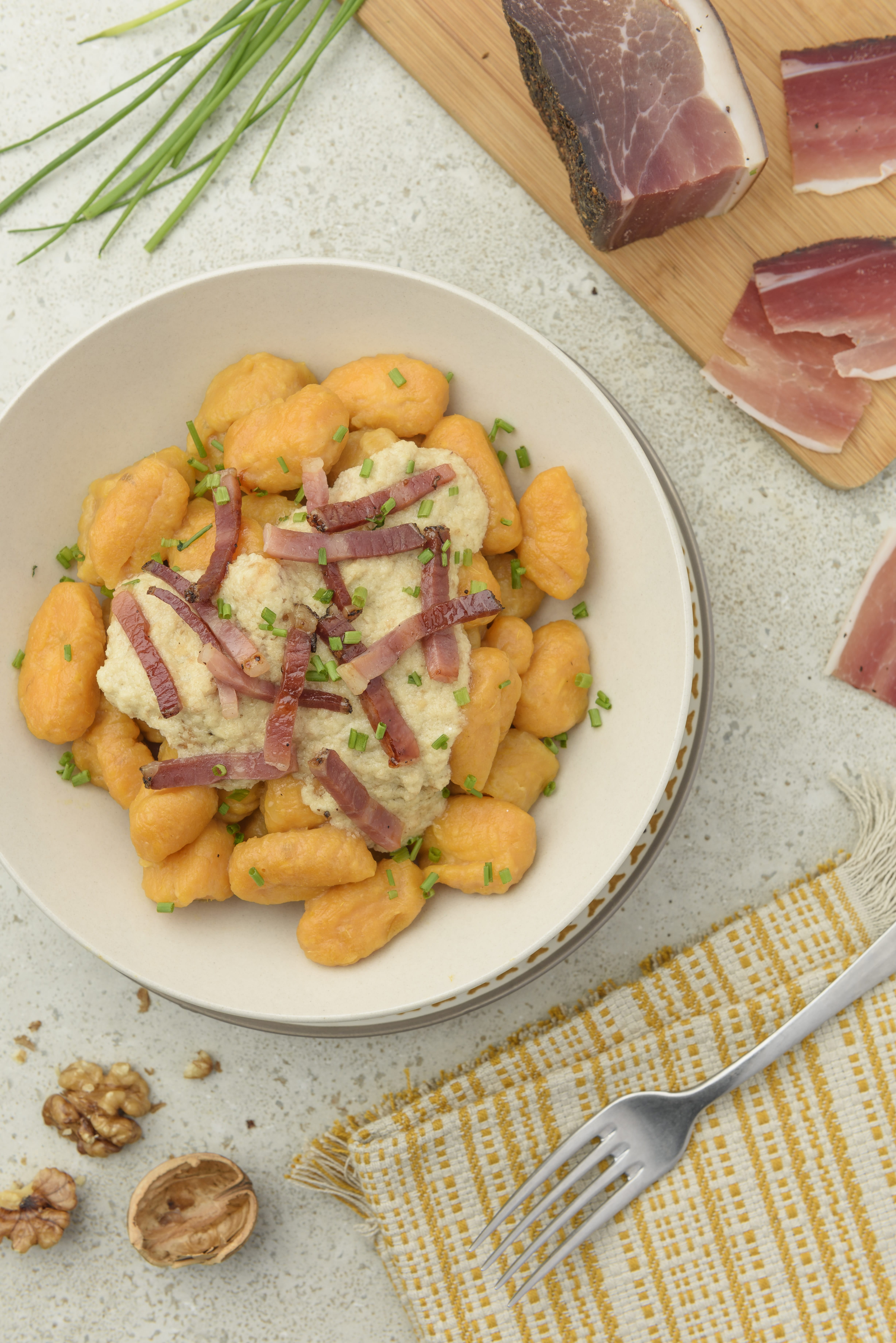 gnocchi di patate dolci serviti su piatto con speck e salsa di noci