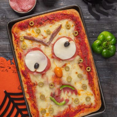 Pizza con ingredienti posizionati per creare il volto di un mostro, perfetta per halloween