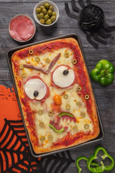 Pizza con ingredienti posizionati per creare il volto di un mostro, perfetta per halloween