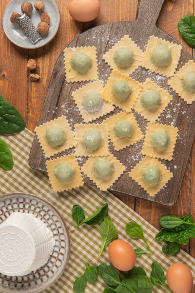 tagliere di legno con ravioli ricotta e spinaci e vari ingredienti