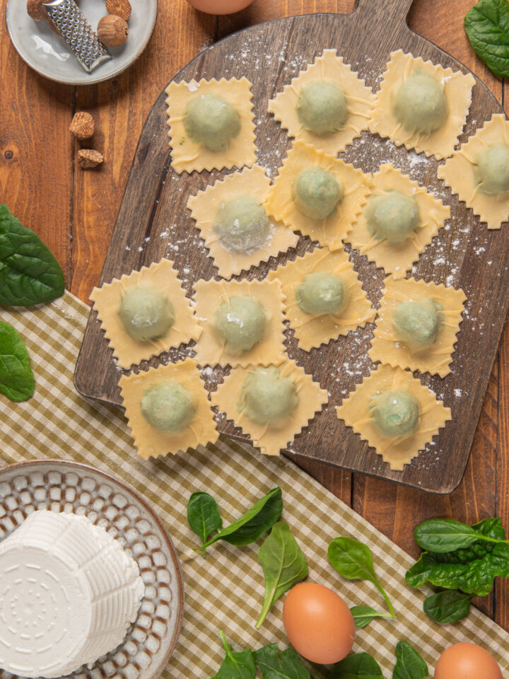 tagliere di legno con ravioli ricotta e spinaci e vari ingredienti