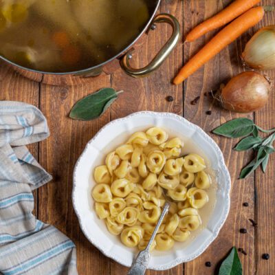 tortellini in brodo in piatto di portata con pentola con brodo e carne