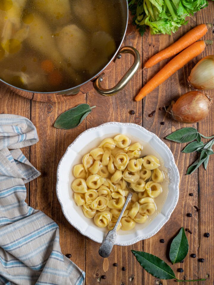 tortellini in brodo in piatto di portata con pentola con brodo e carne