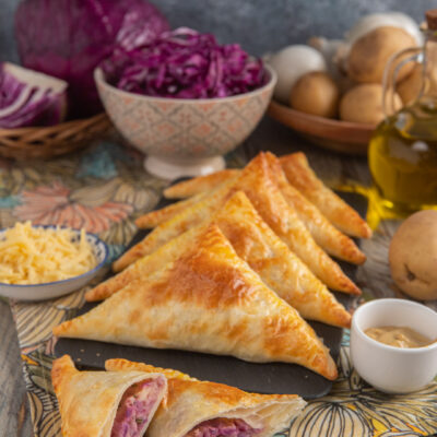 Hand pies vegetariane su piatto rettangolare di ardesia, con cavolo viola e formaggio