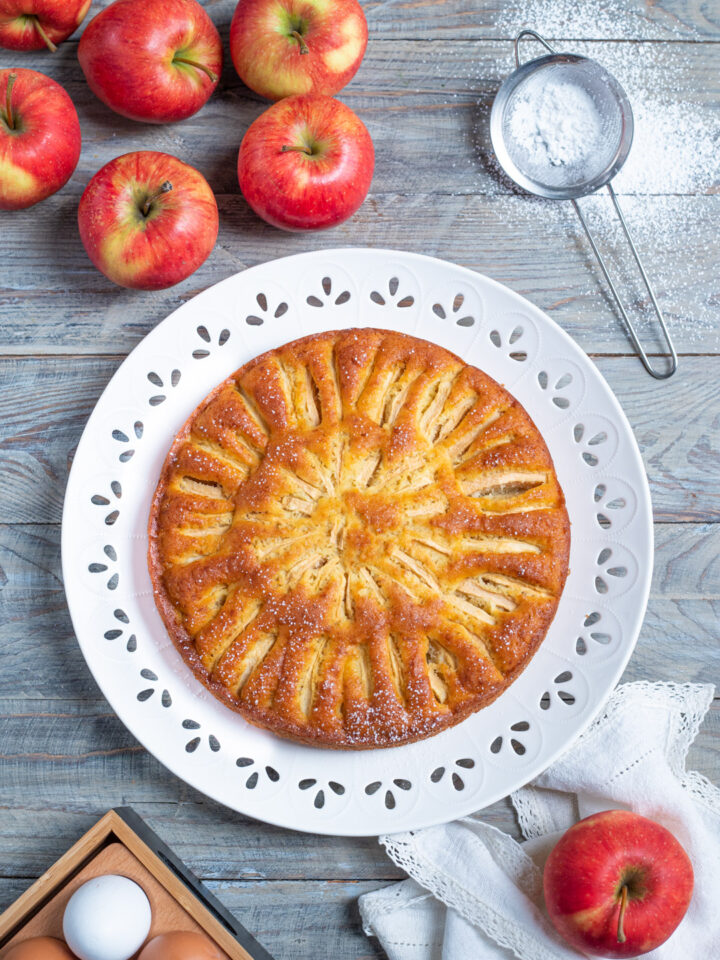 piatto da portata con torta di mele intera, mele e zucchero a velo