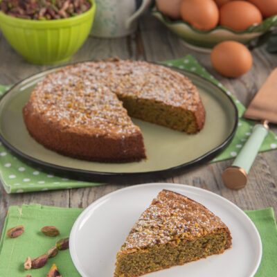 fetta di torta tenerina in primo piato con uova e pistacchi sullo sfondo