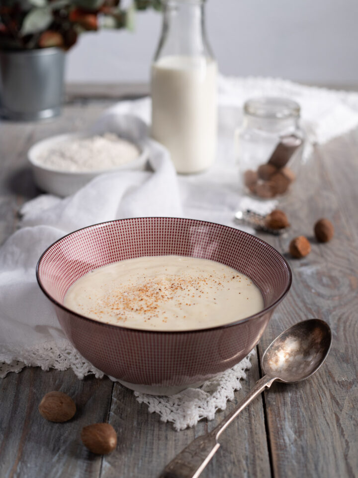 ciotolina con besciamella, cucchiaio e ingredienti sullo sfondo