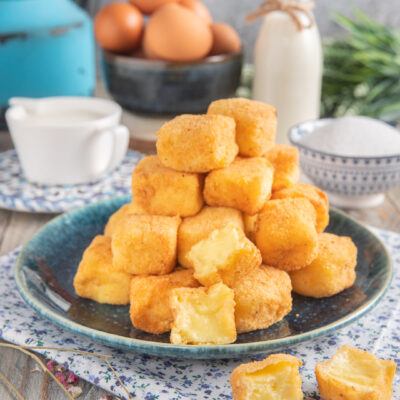 Crema fritta con cubotti a piramide e sullo sfondo uova, zuccheriera, latte e vaso azzurro