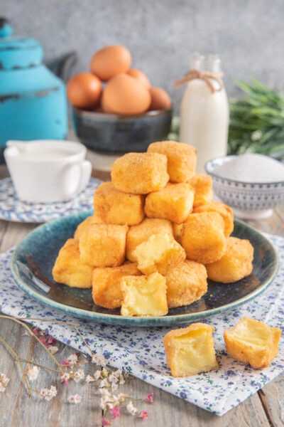 Crema fritta con cubotti a piramide e sullo sfondo uova, zuccheriera, latte e vaso azzurro