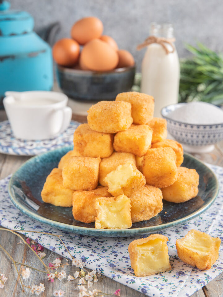 Crema fritta con cubotti a piramide e sullo sfondo uova, zuccheriera, latte e vaso azzurro