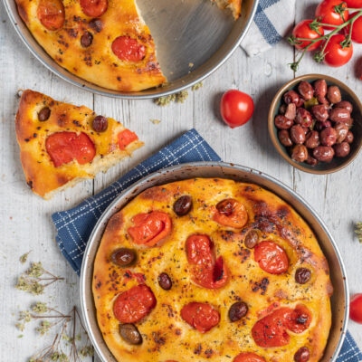 Focaccia barese intera e con fetta tagliata, pomodorini, origano e ciotolina di olive nere