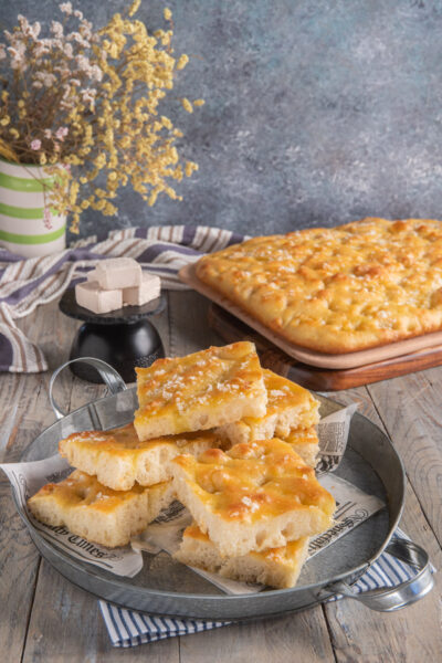 Focaccia genovese su tagliere con fette in primo piano e lievito a cubetti