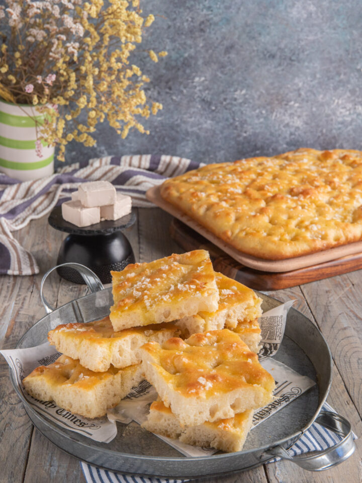 Focaccia genovese su tagliere con fette in primo piano e lievito a cubetti