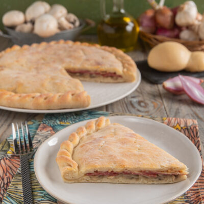 Schiacciata ai funghi e salame con provola con forchetta, tovaglioli colorati e fetta impiattata