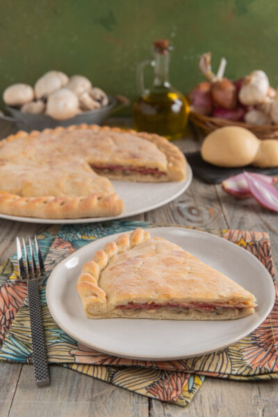 Schiacciata ai funghi e salame con provola con forchetta, tovaglioli colorati e fetta impiattata