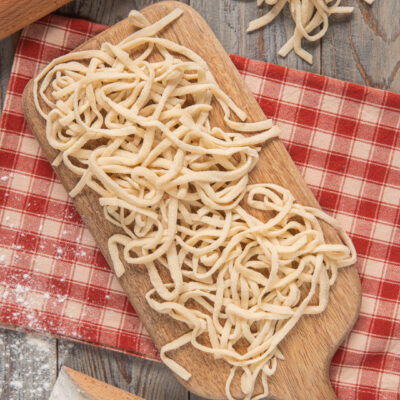 Tonnarelli su tagliere di legno, con mattarello e strofinaccio a quadretti bianchi e rossi