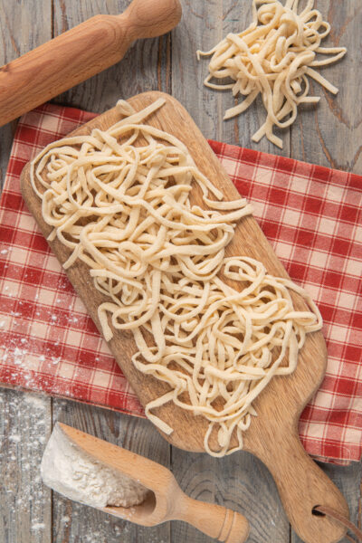 Tonnarelli su tagliere di legno, con mattarello e strofinaccio a quadretti bianchi e rossi