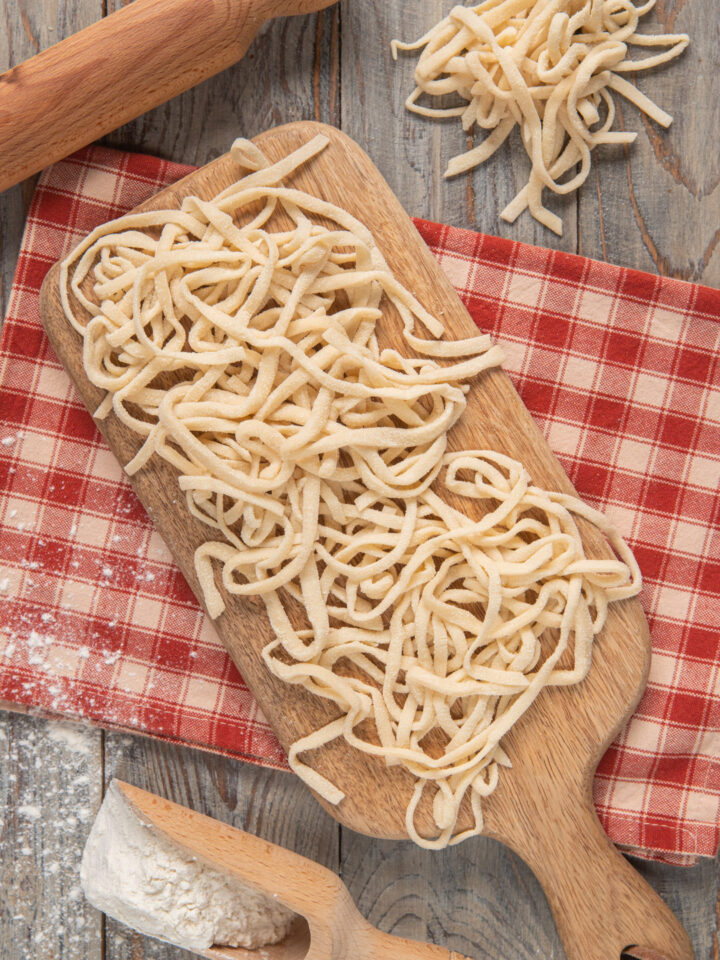 Tonnarelli su tagliere di legno, con mattarello e strofinaccio a quadretti bianchi e rossi