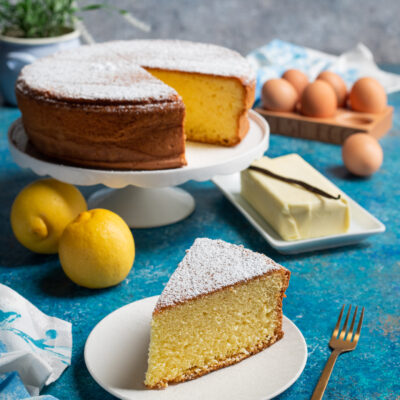 torta margherita su alzatina, fetta di torta in primo piano, burro, uova e limoni