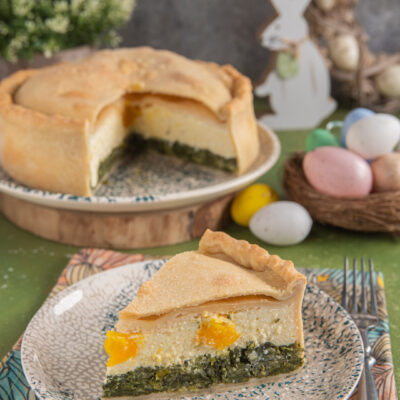 Torta pasqualina con fetta tagliata, uova colorate e coniglio bianco