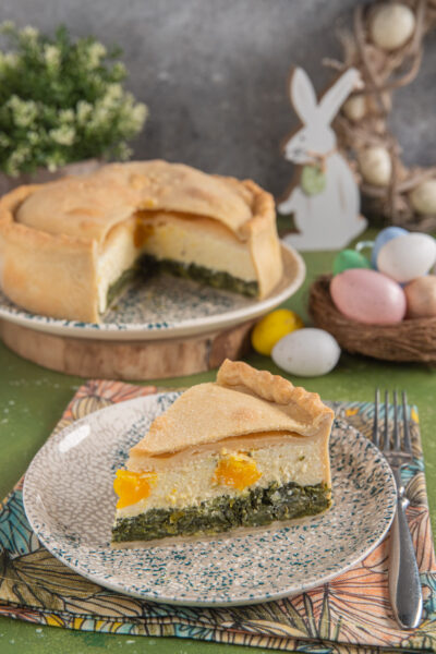 Torta pasqualina con fetta tagliata, uova colorate e coniglio bianco