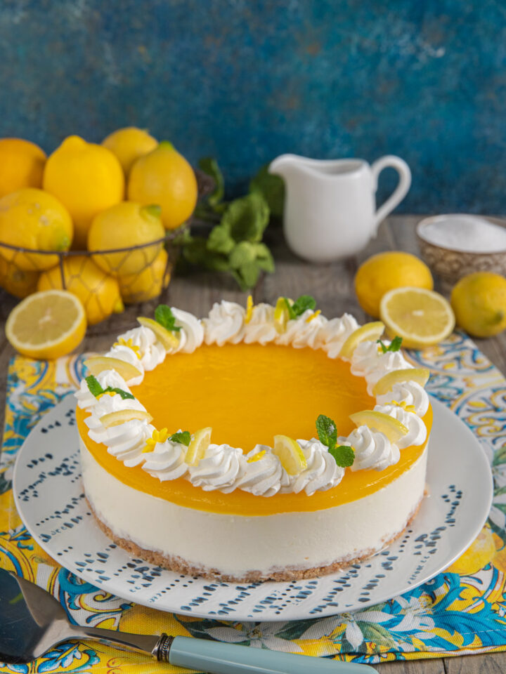 Cheesecake al limone su piatto bianco e azzurro, con cestino di limoni e paletta da dolci