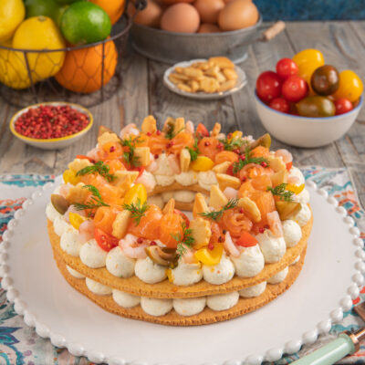 Cream tart salata con salmone su piatto bianco con bordi decorati, pomodorini, uova e agrumi sullo sfondo
