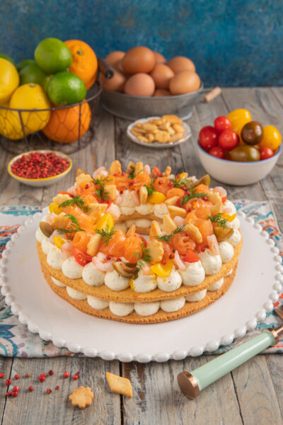 Cream tart salata con salmone su piatto bianco con bordi decorati, pomodorini, uova e agrumi sullo sfondo