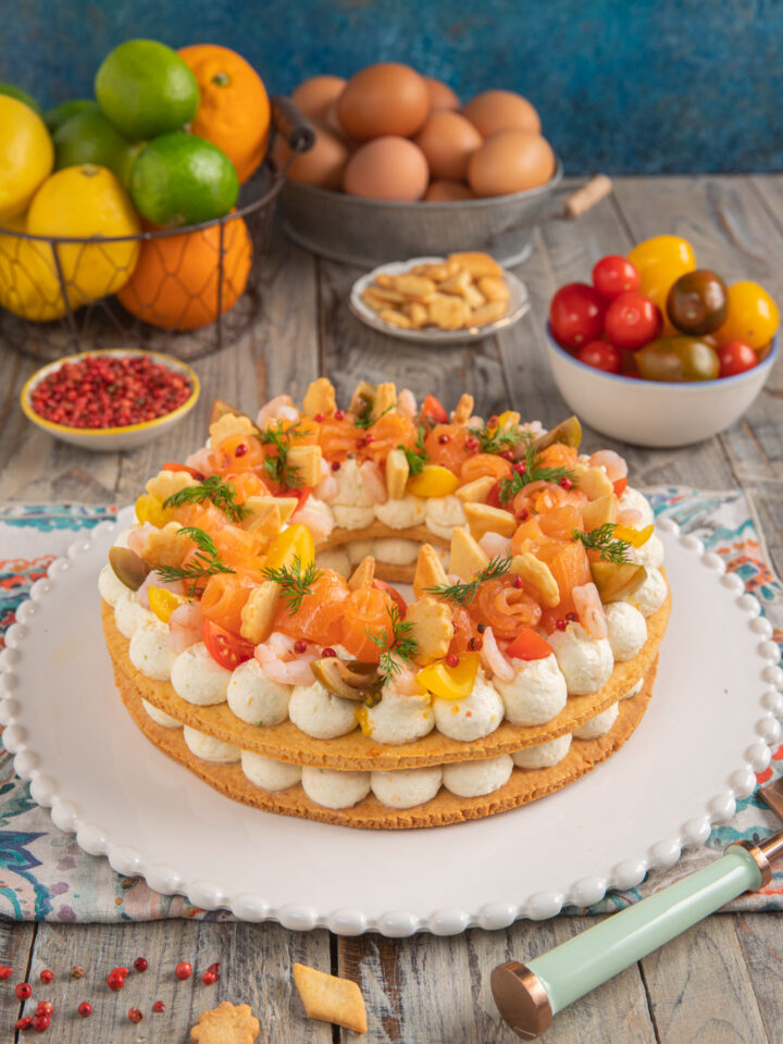 Cream tart salata con salmone su piatto bianco con bordi decorati, pomodorini, uova e agrumi sullo sfondo