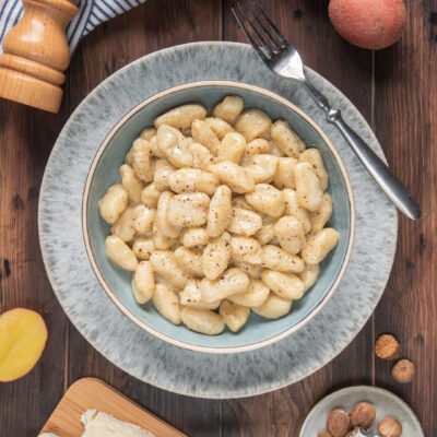 Gnocchi al gorgonzola su piatto grigio con forchetta e macinapepe