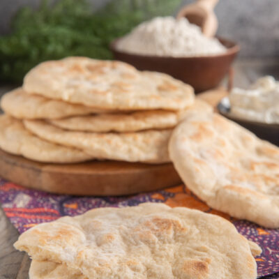 pila di pane naan su tagliere di legno e in primo piano pane naan spezzato