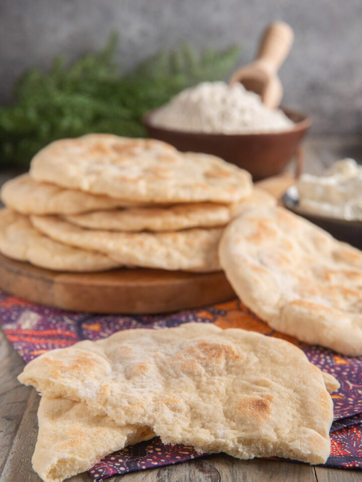 pila di pane naan su tagliere di legno e in primo piano pane naan spezzato