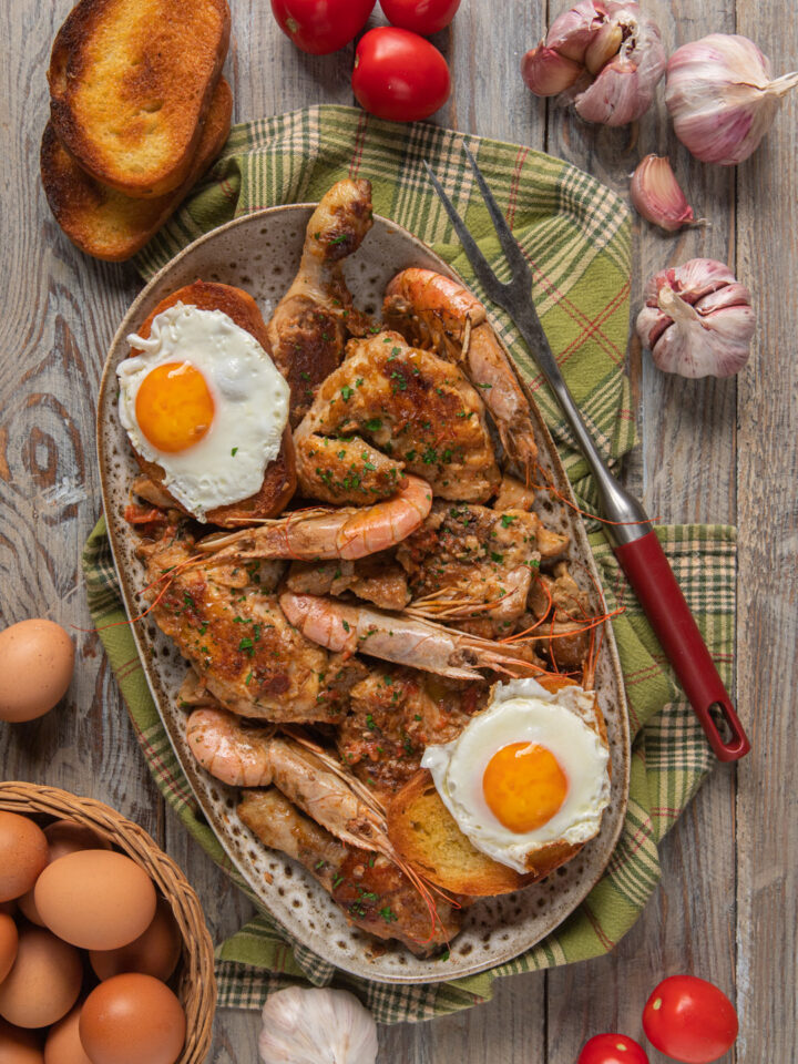 Pollo alla marengo su vassoio ovale, con forcone da carne, uova, testa d'aglio e pane abbrustolito