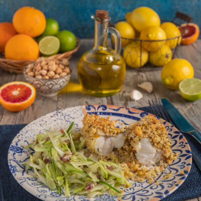 Rana pescatrice agli agrumi con insalata di puntarelle boccetta d'olio, cestino di arance e lime, cestino di limoni e tovaglietta blu