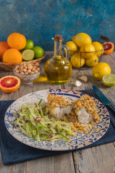Rana pescatrice agli agrumi con insalata di puntarelle boccetta d'olio, cestino di arance e lime, cestino di limoni e tovaglietta blu