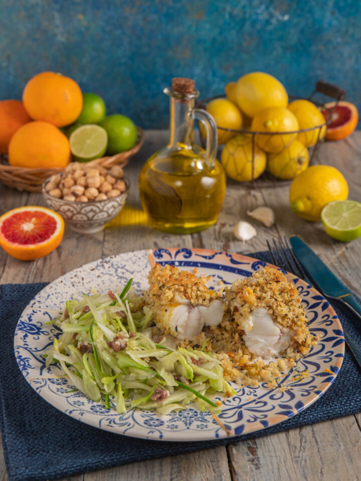 Rana pescatrice agli agrumi con insalata di puntarelle boccetta d'olio, cestino di arance e lime, cestino di limoni e tovaglietta blu