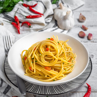 piatto da portata con spaghetti aglio olio e peperoncino e ingredienti sullo sfondo