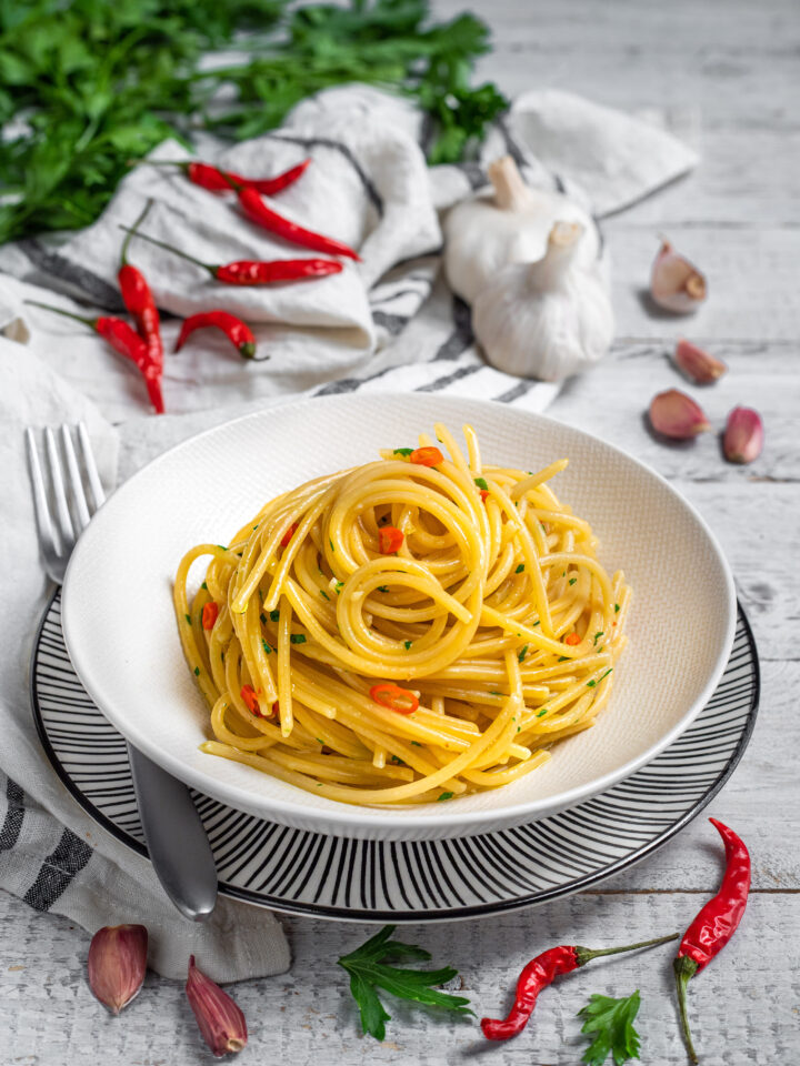 piatto da portata con spaghetti aglio olio e peperoncino e ingredienti sullo sfondo