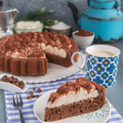 torta al cappuccino con fetta tagliata in primo piano e tazza di caffelatte