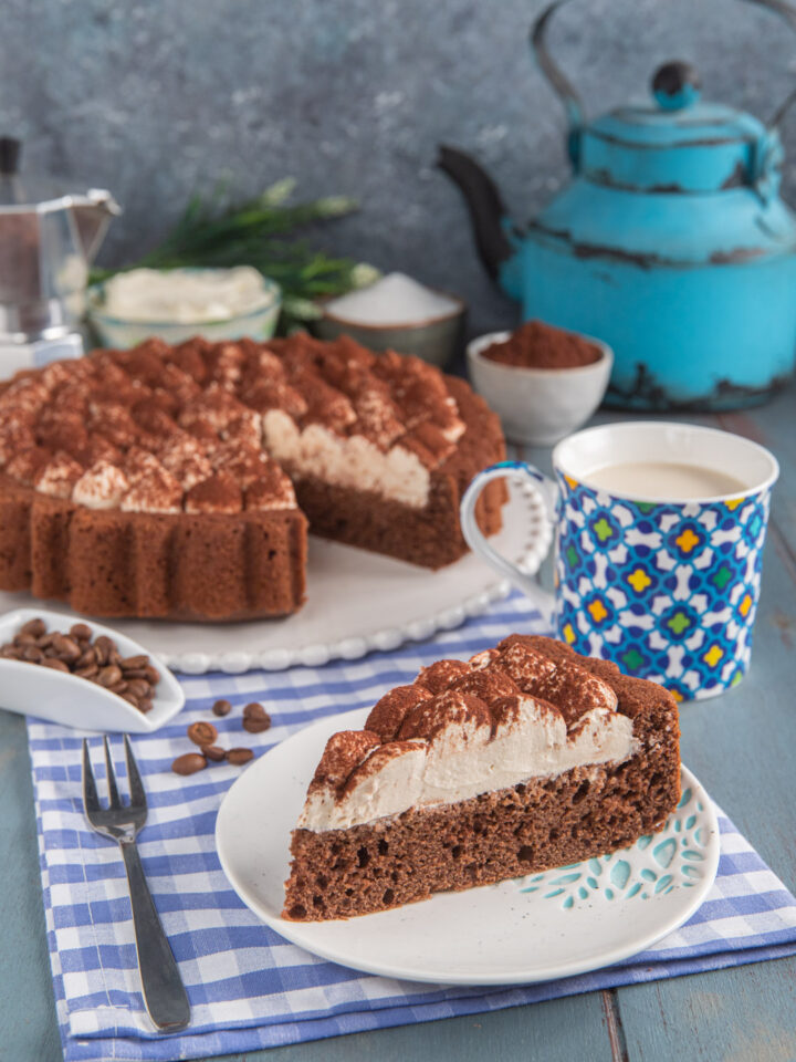 torta al cappuccino con fetta tagliata in primo piano e tazza di caffelatte