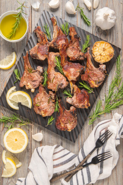 piatto da portata con agnello a scottadito, fette di limone, rosmarino e aglio