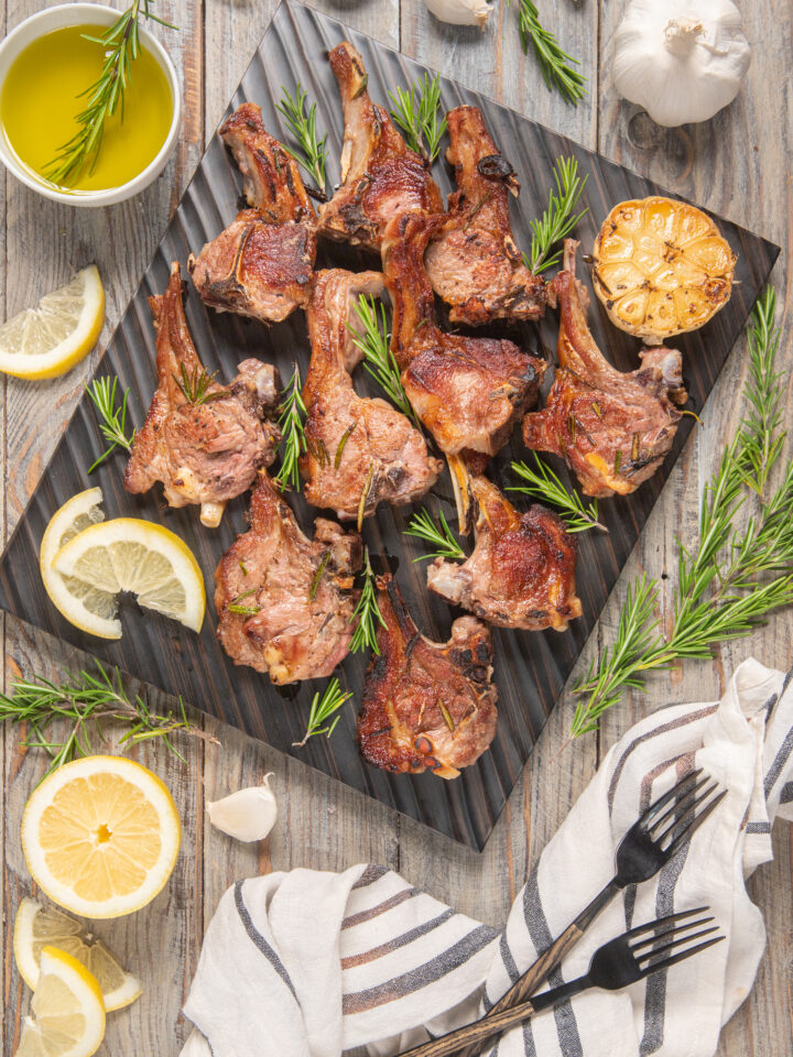 piatto da portata con agnello a scottadito, fette di limone, rosmarino e aglio