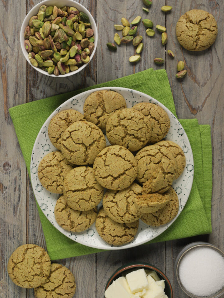 Biscotti al pistacchio su tovagliolo verde con pistacchi interi in ciotolina bianca