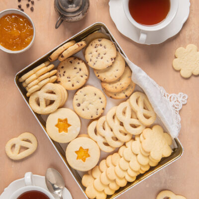 Biscotti senza burro in scatola rettangolare, con tazze di tè e ciotolina di confettura