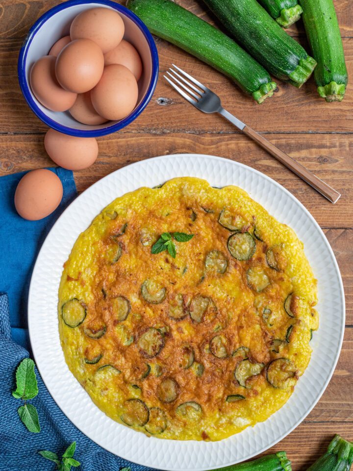 piatto da portata con frittata alle zucchine, uova, forchetta e zucchine intere