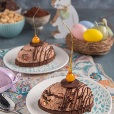 Gelato di Pasqua con sablè al cacao su due piattini, con tovagliette colorate, cestino di uova colorate e coniglietto sullo sfondo