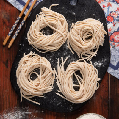 Noodles disposti in 4 nidi su piatto nero, con tovaglietta orientale e bacchette cinesi