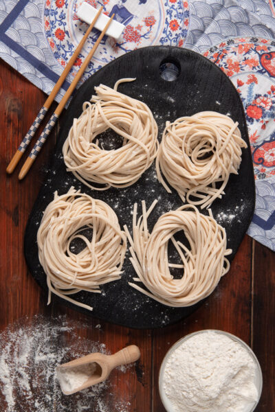 Noodles disposti in 4 nidi su piatto nero, con tovaglietta orientale e bacchette cinesi